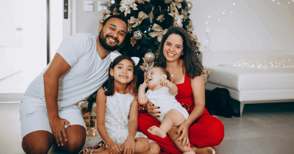A newborn baby being held by family in a cozy living room decorated for Christmas with warm lights and holiday decorations.