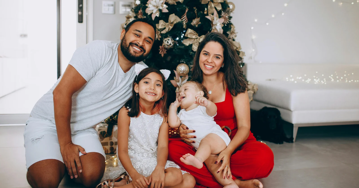 A newborn baby being held by family in a cozy living room decorated for Christmas with warm lights and holiday decorations.