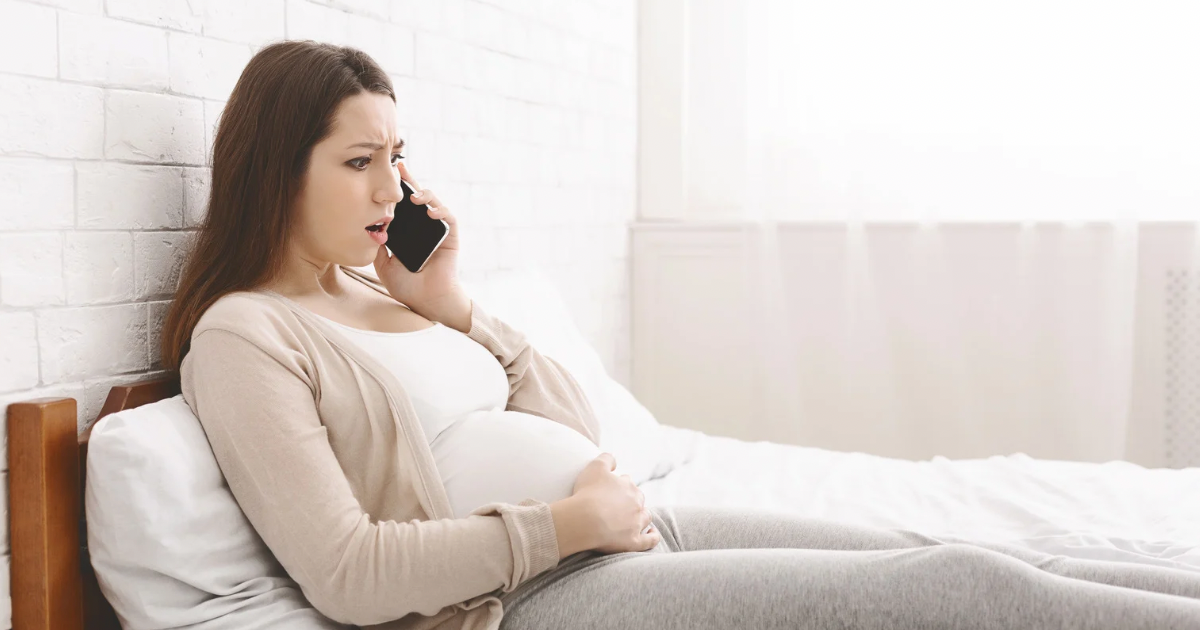 Pregnant mom sitting on her bed, on the phone, verifying insurance benefits for lactation and breastfeeding support.